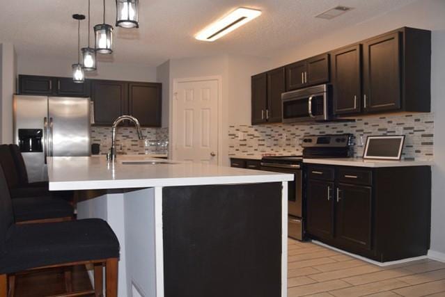 kitchen with backsplash, a kitchen island with sink, sink, and stainless steel appliances