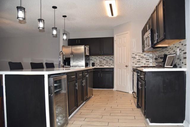 kitchen featuring hanging light fixtures, beverage cooler, backsplash, appliances with stainless steel finishes, and light wood-type flooring