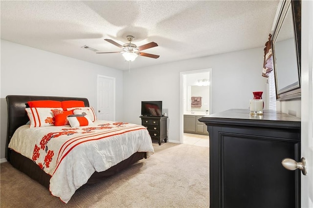 bedroom featuring ceiling fan, light colored carpet, a textured ceiling, and ensuite bath