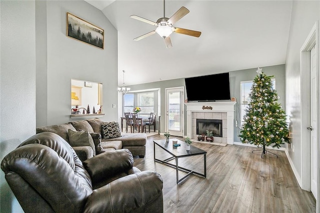 living room featuring hardwood / wood-style floors, ceiling fan with notable chandelier, vaulted ceiling, and a tiled fireplace