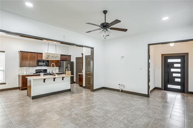 kitchen with ceiling fan, a breakfast bar area, decorative backsplash, a center island with sink, and black appliances