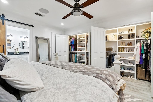 bedroom featuring a barn door, light hardwood / wood-style flooring, and ceiling fan