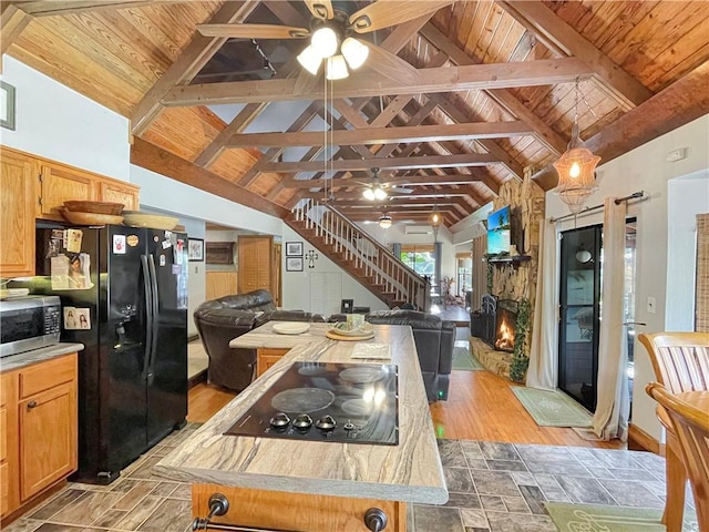 kitchen with a stone fireplace, wood ceiling, beamed ceiling, ceiling fan, and black appliances