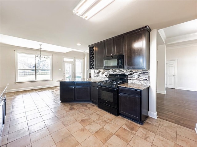 kitchen with tasteful backsplash, light stone counters, ornamental molding, black appliances, and an inviting chandelier