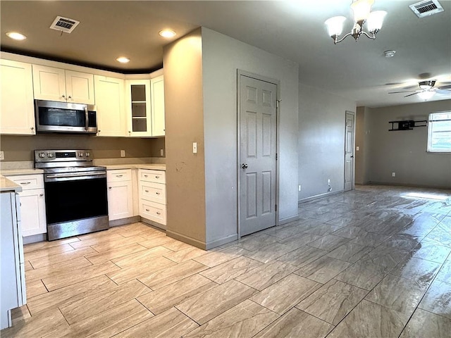 kitchen with white cabinets, appliances with stainless steel finishes, ceiling fan with notable chandelier, and pendant lighting