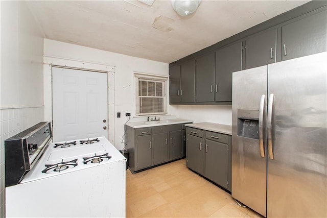 kitchen featuring light floors, gas range gas stove, gray cabinets, light countertops, and stainless steel refrigerator with ice dispenser