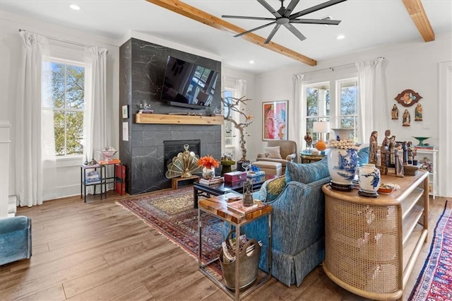 living room featuring beamed ceiling, hardwood / wood-style floors, a fireplace, and ceiling fan