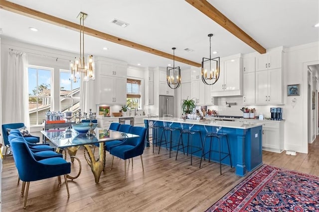 kitchen featuring a breakfast bar, a kitchen island, beam ceiling, light hardwood / wood-style floors, and white cabinetry