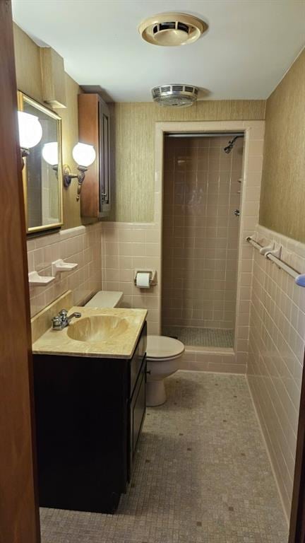 bathroom featuring tile patterned floors, toilet, tile walls, a tile shower, and vanity