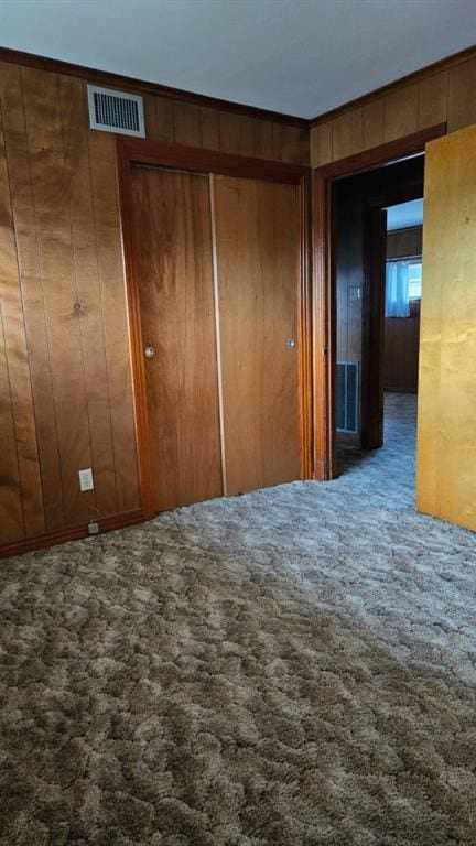 unfurnished bedroom featuring a closet, wood walls, and carpet