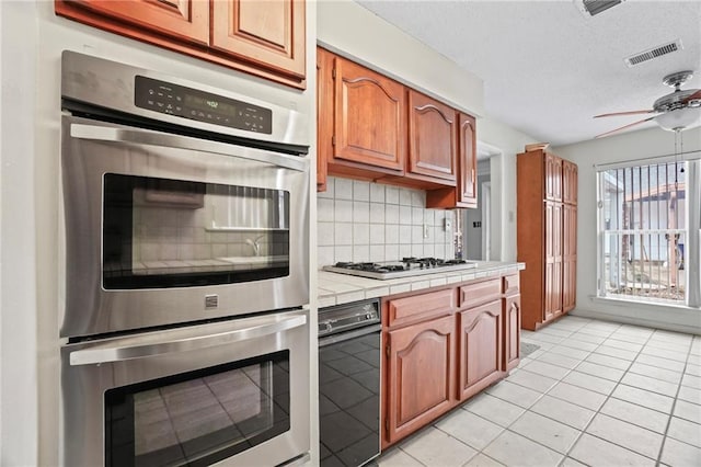 kitchen featuring tile countertops, white gas stovetop, light tile patterned floors, tasteful backsplash, and stainless steel double oven