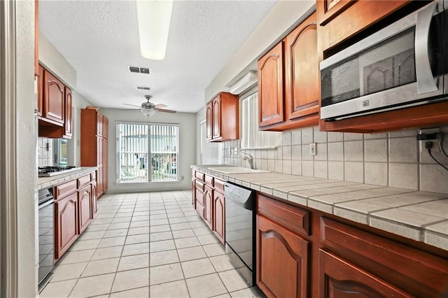 kitchen with ceiling fan, tile counters, stainless steel appliances, tasteful backsplash, and light tile patterned floors