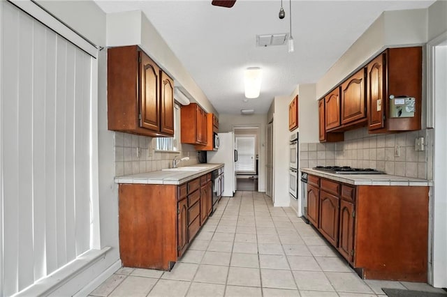 kitchen with decorative backsplash, ceiling fan, tile countertops, dishwasher, and stainless steel gas stovetop