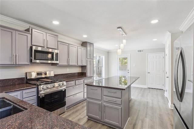 kitchen with gray cabinets, pendant lighting, stainless steel appliances, and light hardwood / wood-style flooring