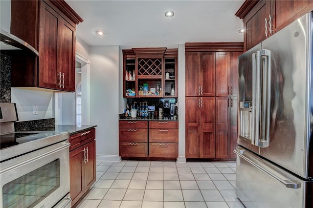 kitchen featuring electric range, wall chimney exhaust hood, dark stone counters, high quality fridge, and light tile patterned floors