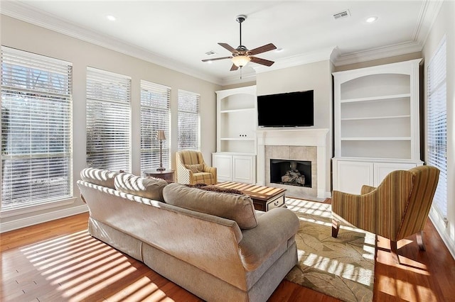 living area featuring light wood finished floors, visible vents, a tile fireplace, ornamental molding, and built in shelves