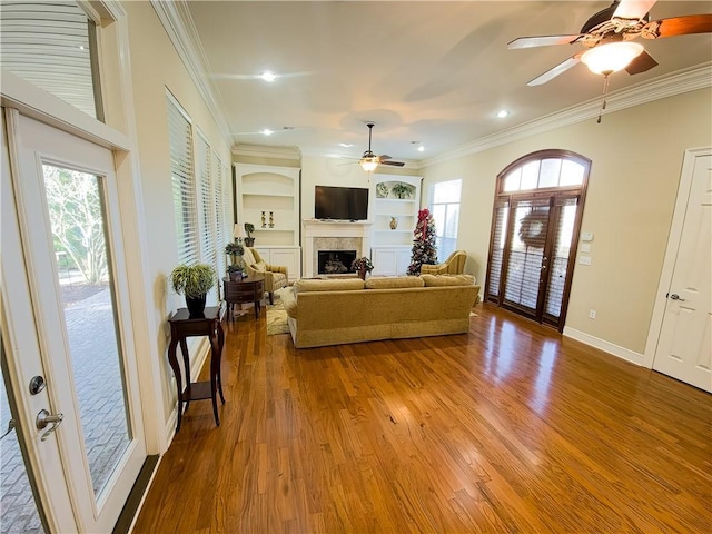 living room with hardwood / wood-style floors, crown molding, a fireplace, and built in features