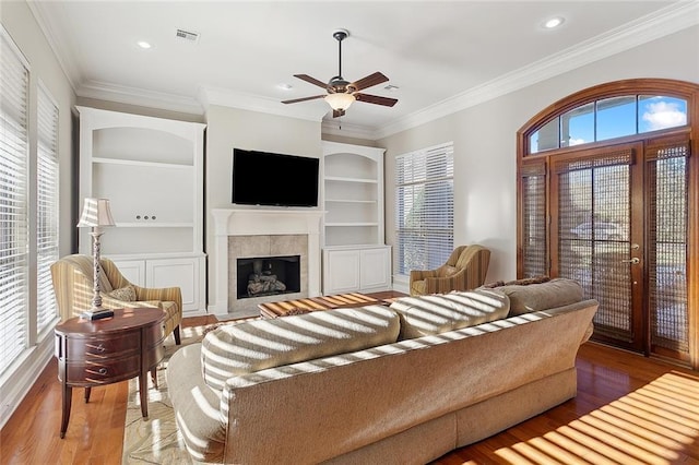 living area with crown molding, a tile fireplace, wood finished floors, and built in features