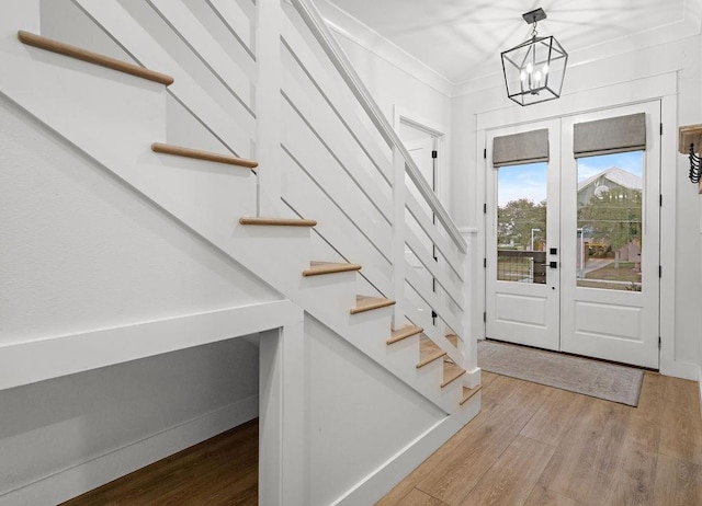 foyer featuring french doors, crown molding, light hardwood / wood-style flooring, and a notable chandelier