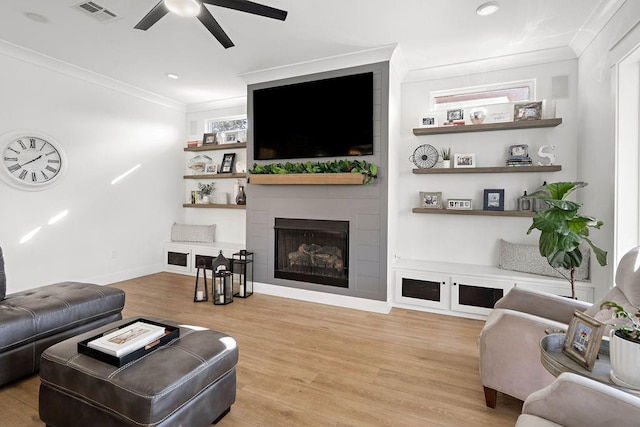 living room featuring a tile fireplace, ornamental molding, ceiling fan, and light wood-type flooring