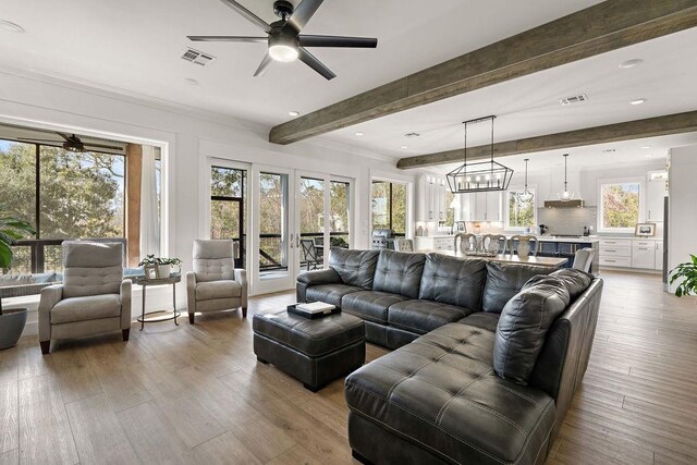 living room featuring ceiling fan with notable chandelier, ornamental molding, beam ceiling, and hardwood / wood-style floors