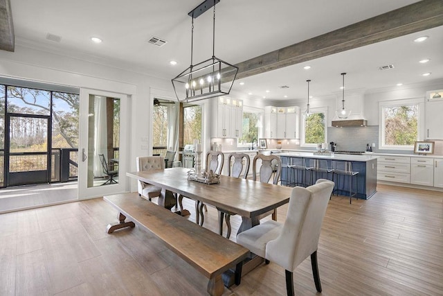 dining space with beamed ceiling, crown molding, plenty of natural light, and light hardwood / wood-style flooring