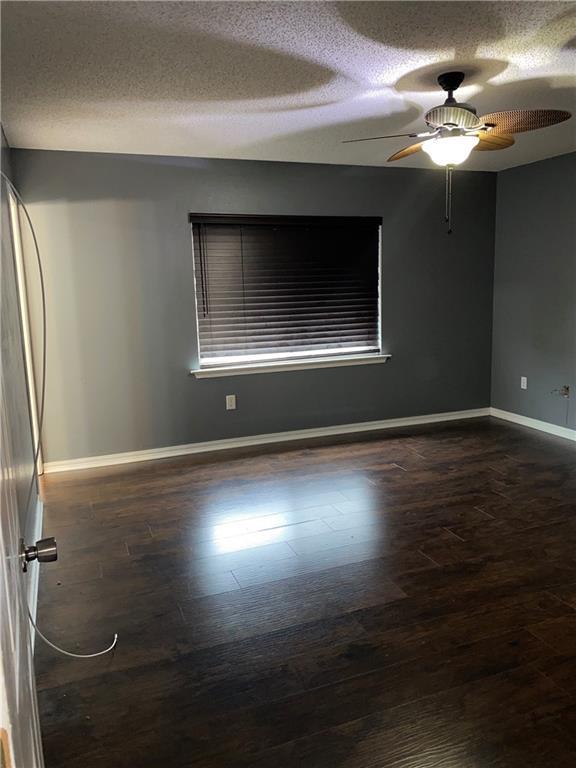 empty room with a textured ceiling, ceiling fan, and dark wood-type flooring