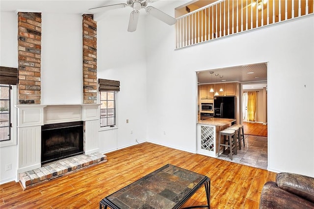 living room featuring ceiling fan, plenty of natural light, light hardwood / wood-style flooring, and a brick fireplace