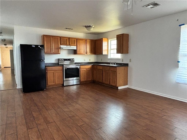 kitchen with dark countertops, stainless steel electric range oven, dark wood-type flooring, freestanding refrigerator, and under cabinet range hood