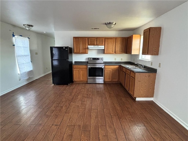 kitchen with dark countertops, freestanding refrigerator, stainless steel range with electric cooktop, under cabinet range hood, and a sink