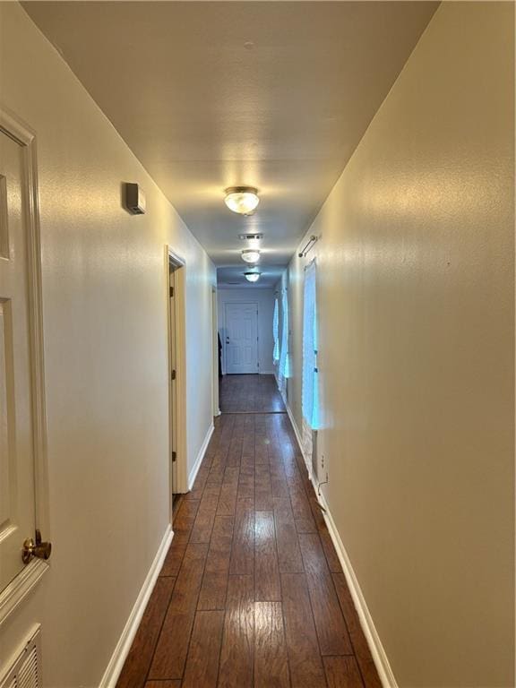 hallway featuring dark wood-style flooring, visible vents, and baseboards