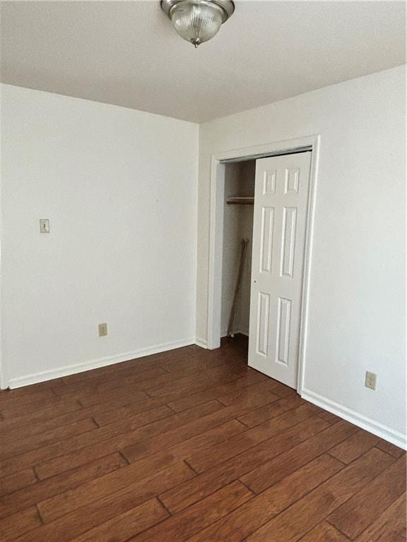 unfurnished bedroom featuring wood-type flooring, baseboards, and a closet