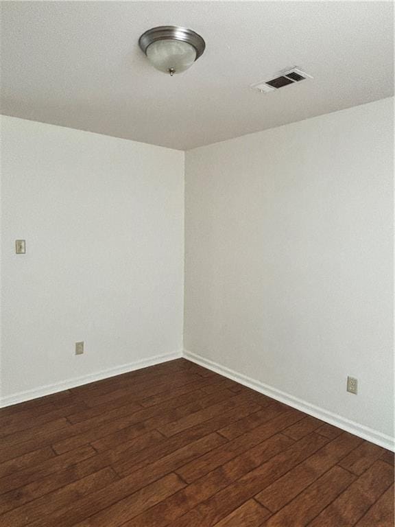 spare room featuring dark wood-style floors, visible vents, and baseboards