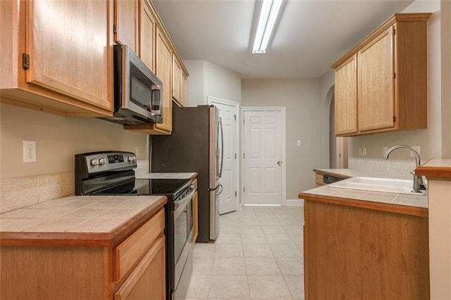 kitchen with appliances with stainless steel finishes, sink, tile countertops, and light tile patterned floors