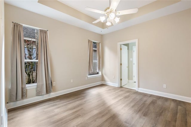 empty room with ceiling fan, wood-type flooring, and a tray ceiling