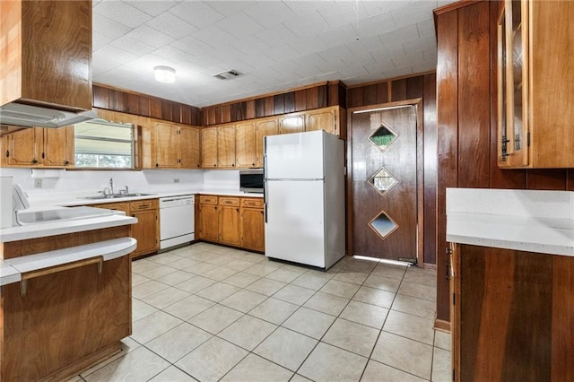 kitchen featuring wooden walls, sink, light tile patterned floors, and white appliances