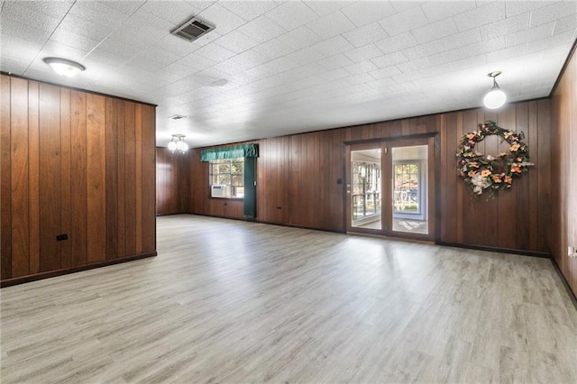 unfurnished room featuring wooden walls, light hardwood / wood-style flooring, and a notable chandelier