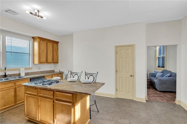 kitchen featuring a sink, stainless steel gas stovetop, a kitchen bar, a center island, and light stone counters