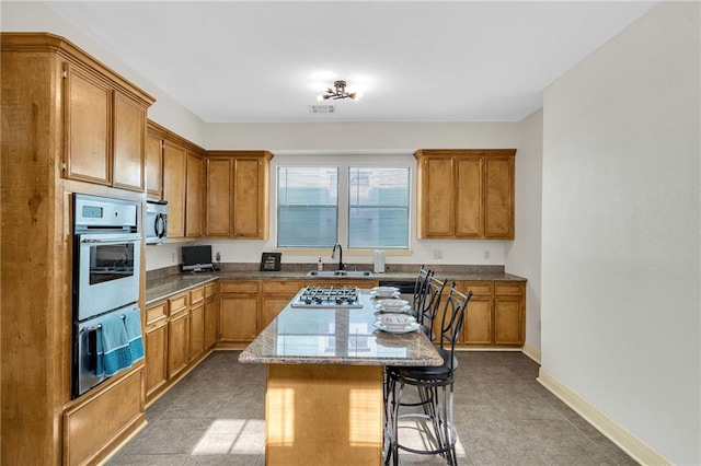 kitchen with sink, a breakfast bar, appliances with stainless steel finishes, a center island, and stone countertops