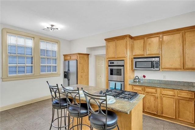 kitchen with a kitchen breakfast bar, light stone counters, stainless steel appliances, tile patterned flooring, and a kitchen island