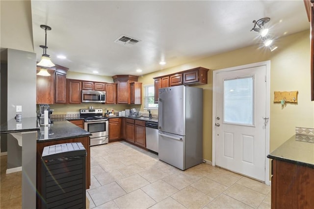 kitchen with kitchen peninsula, dark stone counters, stainless steel appliances, sink, and pendant lighting