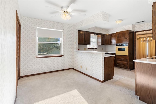 kitchen with light carpet, oven, ceiling fan with notable chandelier, hanging light fixtures, and kitchen peninsula