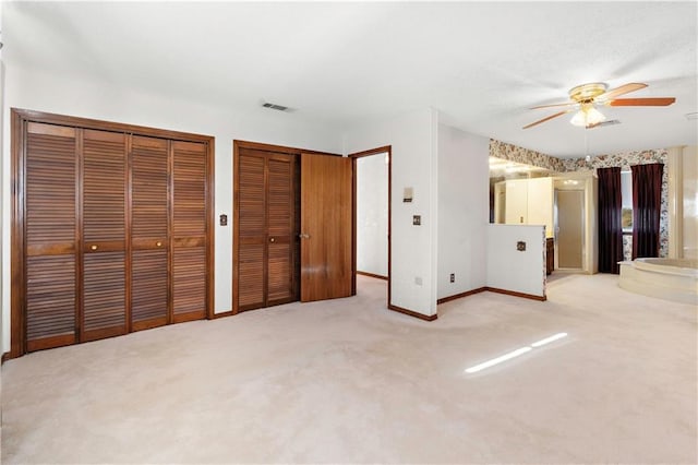 unfurnished bedroom with ceiling fan, light colored carpet, and two closets