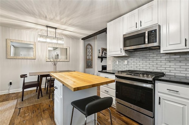 kitchen with butcher block countertops, pendant lighting, a breakfast bar area, white cabinets, and appliances with stainless steel finishes