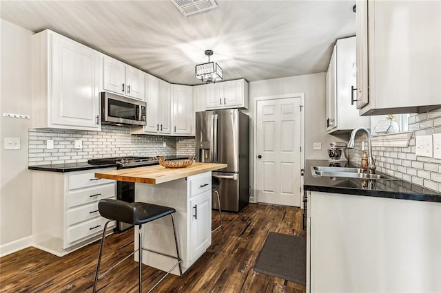 kitchen featuring stainless steel appliances, white cabinetry, and butcher block counters