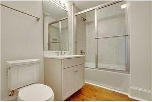 full bathroom with hardwood / wood-style flooring, vanity, enclosed tub / shower combo, and toilet