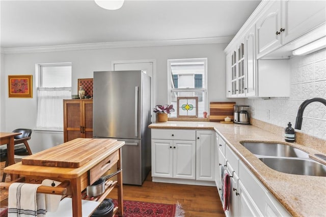 kitchen featuring crown molding, sink, light stone counters, white cabinetry, and stainless steel refrigerator