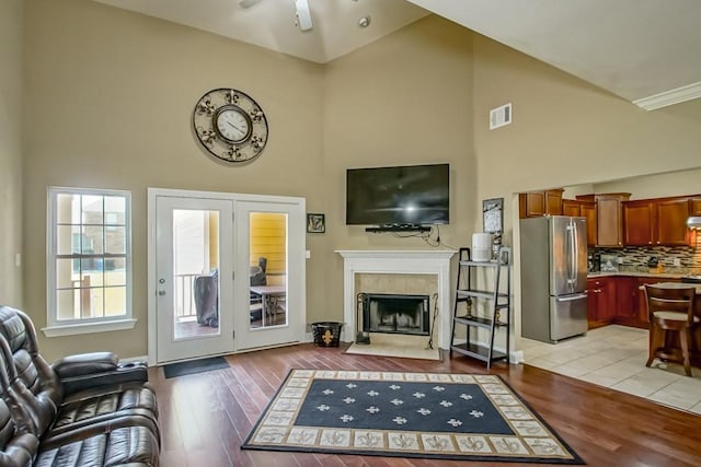 living room with a tile fireplace, light wood-type flooring, high vaulted ceiling, and ceiling fan