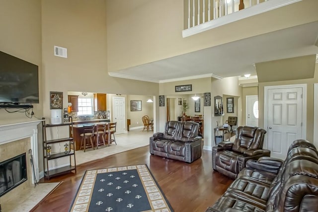 living room featuring a tiled fireplace, wood-type flooring, and a high ceiling