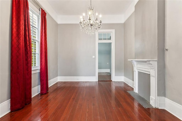 unfurnished living room featuring hardwood / wood-style floors, baseboards, a healthy amount of sunlight, and a chandelier